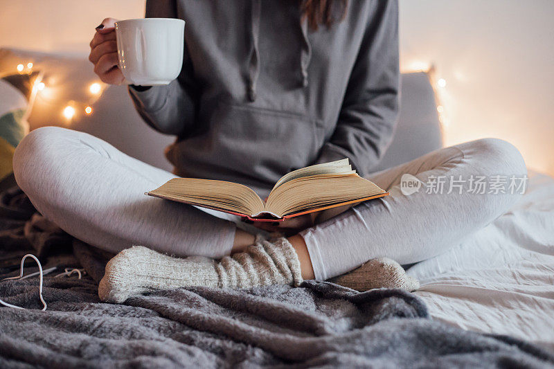 女孩喝着热茶，在床上看书