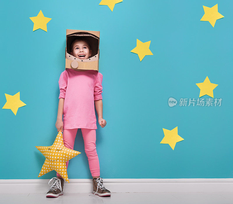 一个穿着宇航员服装的小女孩正在玩耍并梦想成为一名宇航员。一个有趣的孩子的肖像，背景是亮蓝色的墙壁和黄色的星星。