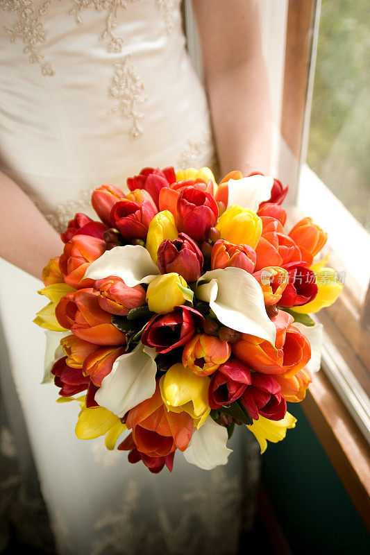 美丽的新娘手捧鲜花站在窗前
