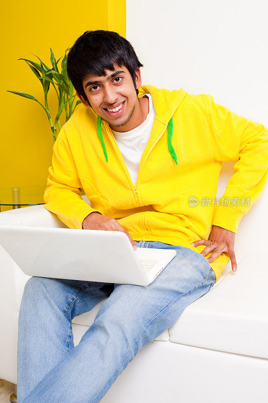 年轻的印度少年愉快的笔记本电脑坐在沙发上
