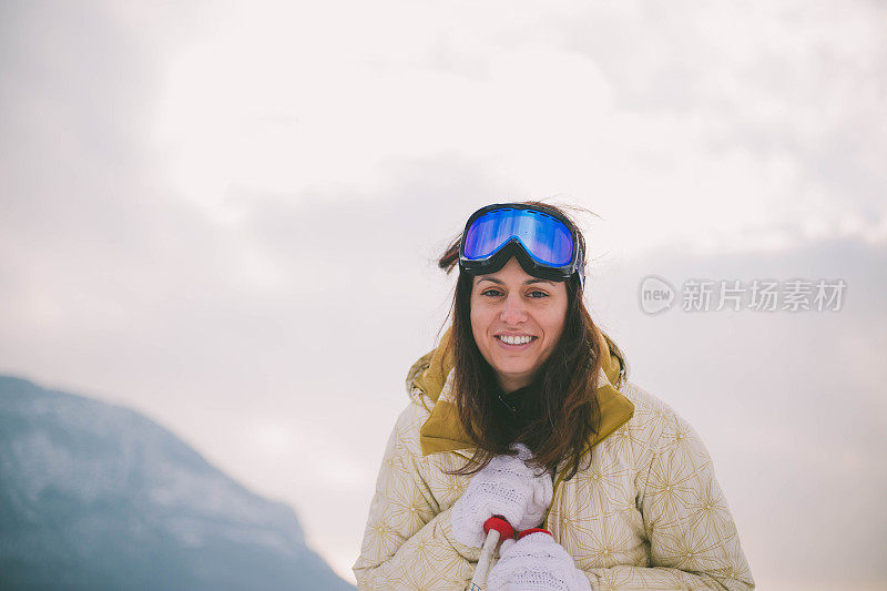 近景美丽的年轻女子在冬天的衣服站在一边，手拿木棍的背景雪山