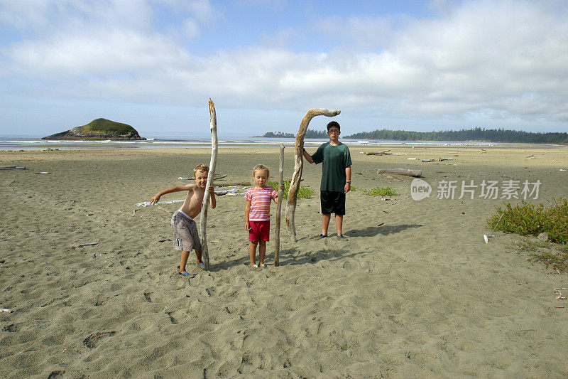 三个孩子在海滩上抱着浮木的广角镜头。