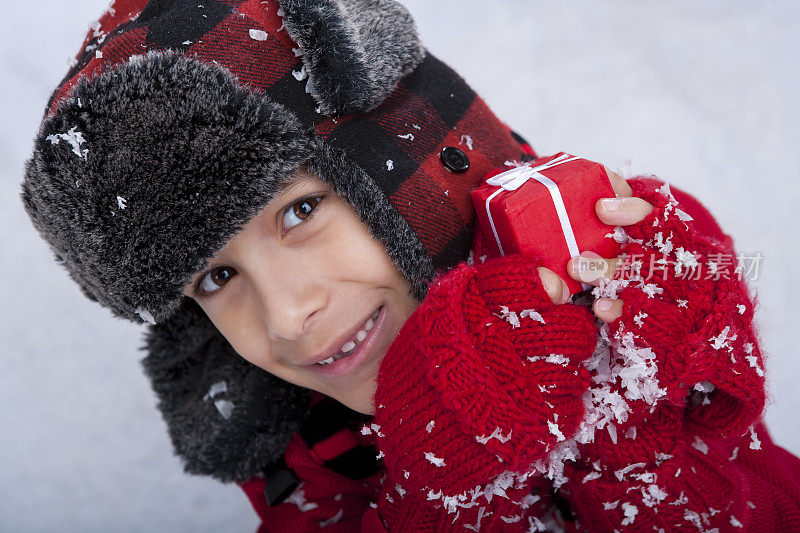 小男孩坐在雪地里拿着圣诞礼物