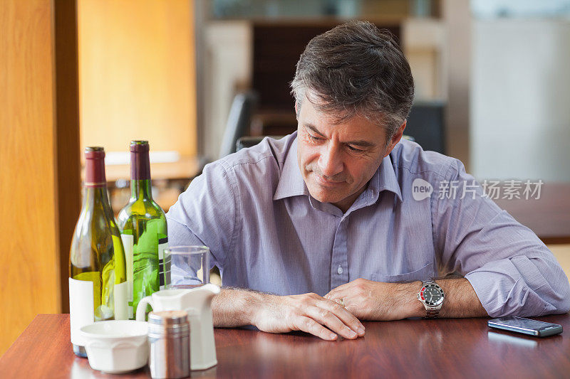 一个拿着两个空酒瓶坐在餐厅里的男人