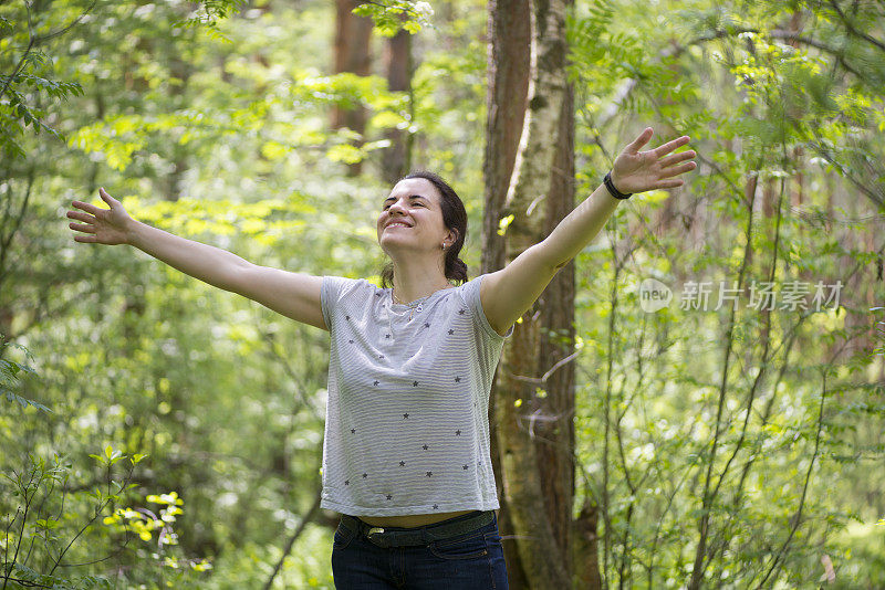 快乐的年轻美丽的女人在森林里举起双手享受自由