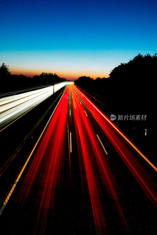 德国盖尔森基兴A2高速公路的长曝光图像，背景是红色和白色的光迹和彩色的日落