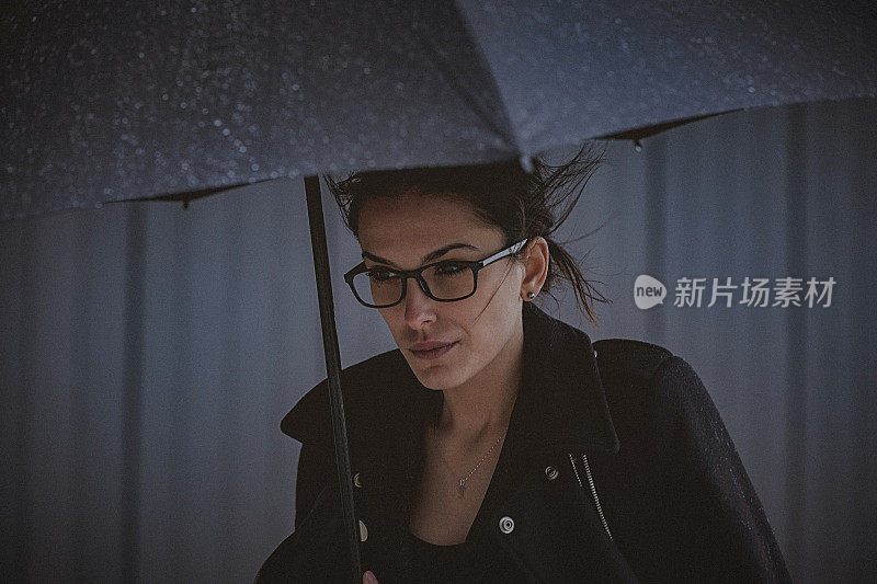 一名年轻女子撑着伞，在寒冷的秋日里在风雨中行走。