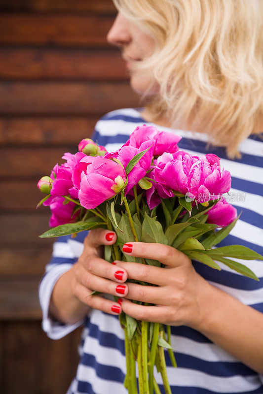 一束美丽的深粉色牡丹在女人的手在一个木制的背景。手里拿着一束花。条纹。夏天的时间。