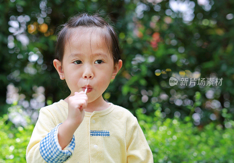 小女孩喜欢在公园里吃棒棒糖。