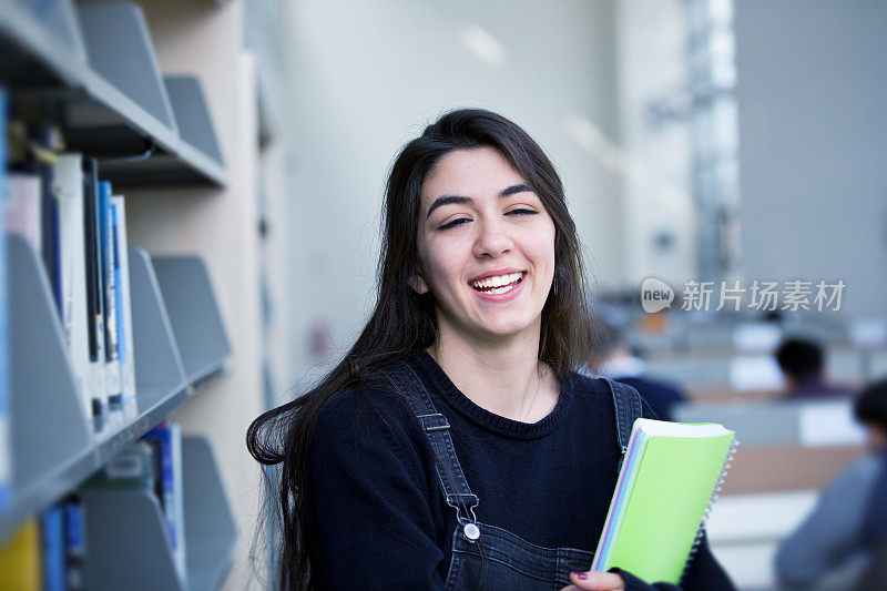 微笑的女学生在图书馆拿着书的肖像