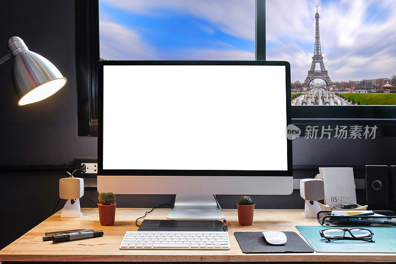 平面设计师的工作空间配备了一个手写板，一台电脑和白色背景的文字与美丽的巴黎城市从窗口