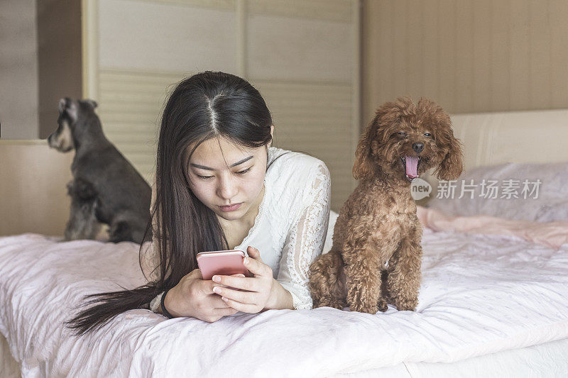 一个女人一边玩智能手机，一边看着她的宠物