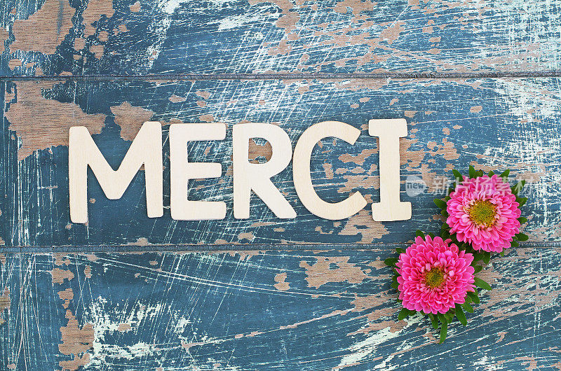 用木制字母和粉色雏菊写的Merci(法语的意思是谢谢)