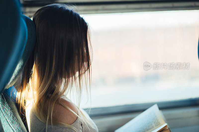 一个女人乘火车旅行，坐在靠近窗户的地方看书。