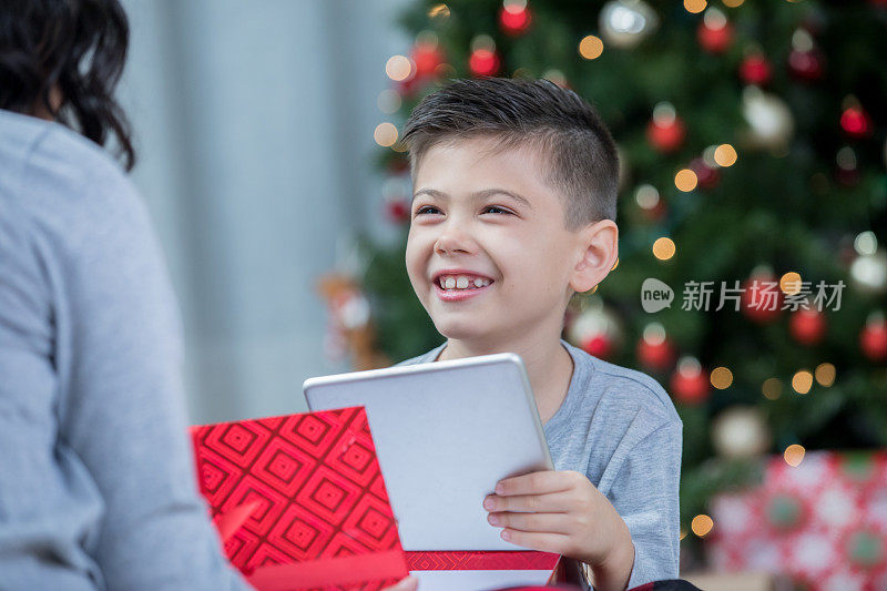 圣诞节早晨，快乐的小男孩打开数码平板电脑后的笑容