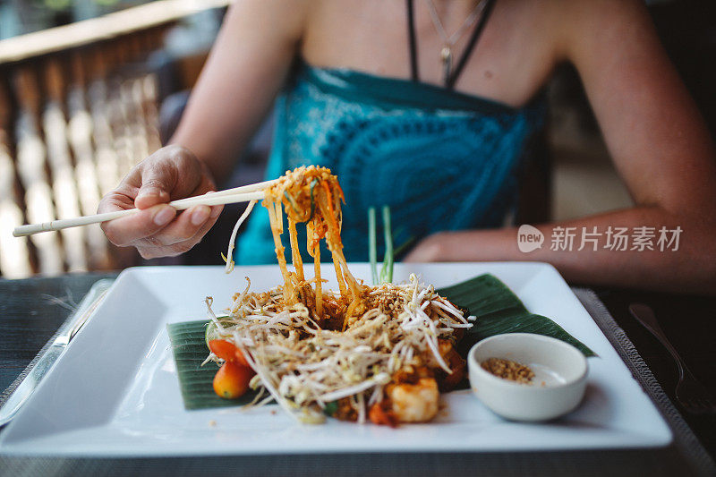 一个年轻女子在海滩酒吧吃泰式炒河粉