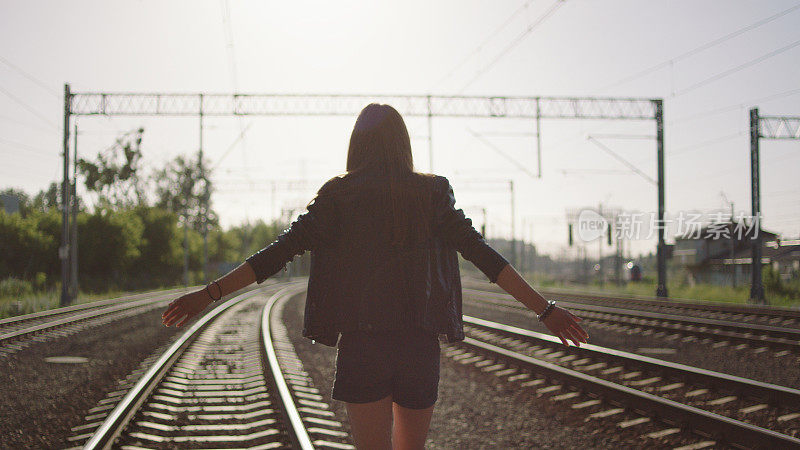 年轻女子在铁路上行走。保持平衡。摇滚风格。