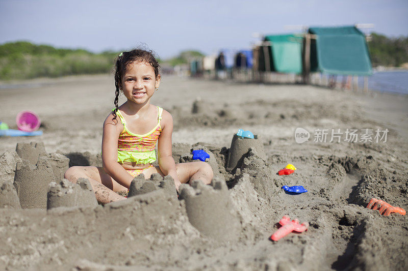 拉丁裔女孩坐在沙上用桶和铲子建沙堡。