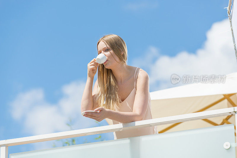 阳台上有个年轻貌美的女人，端着一杯咖啡。金发。