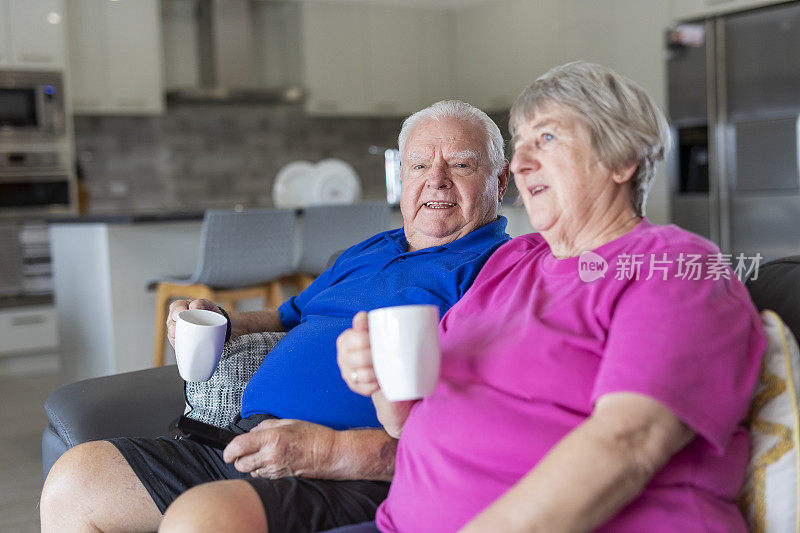 老夫妇一边在沙发上看电视一边喝茶或喝咖啡