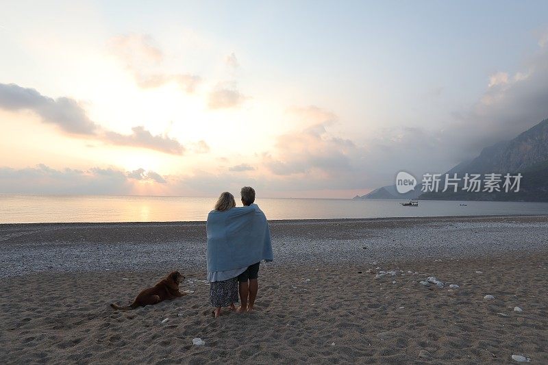 日出时分，一对夫妇带着狗在海滩上散步