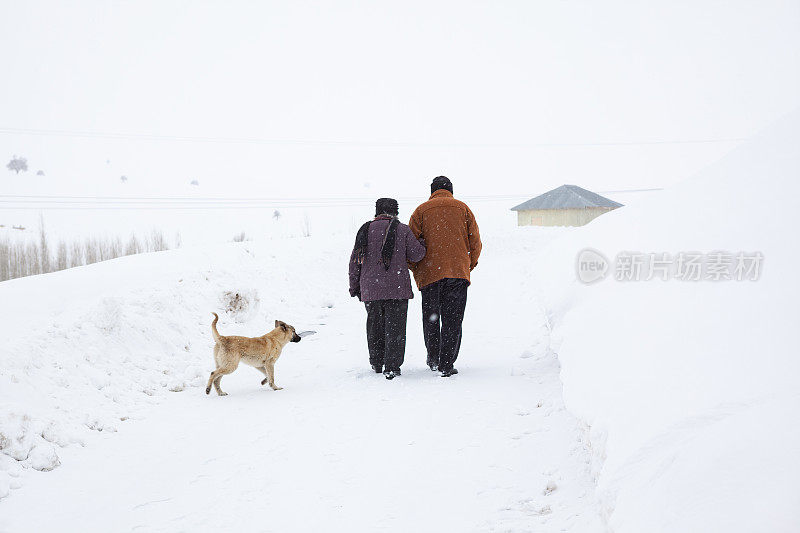 一对老年夫妇在下雪的乡村路上穿着暖和的衣服