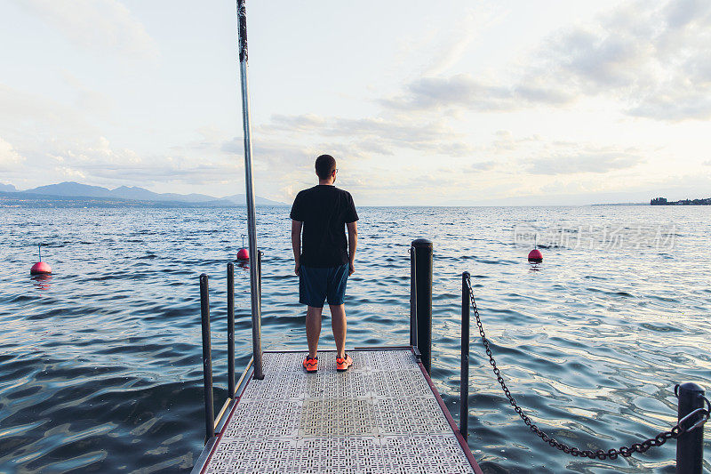 男子呆在码头上欣赏日落在山上的湖在瑞士