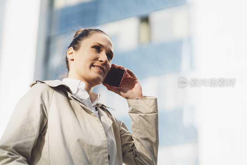 年轻的女商人穿着风衣在外面打电话