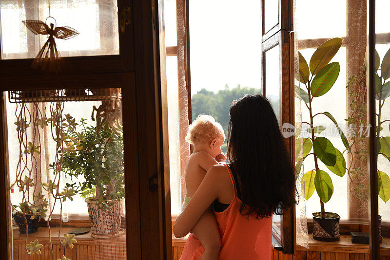 母亲抱着婴儿望着窗外。