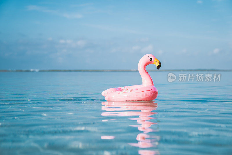 充气粉红色火烈鸟漂浮在透明的绿松石海。蓝色的天空，很少有云的背景。