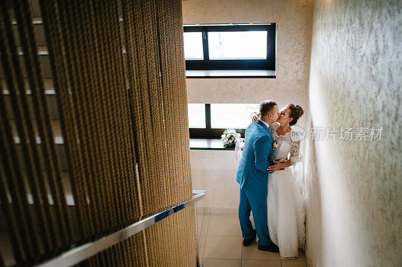 新娘和新郎靠近窗户。第一次会议。新婚夫妇亲吻在室内。新婚快乐。