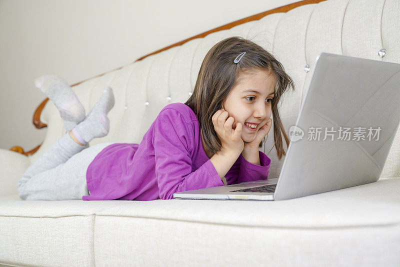 在家的女孩通过互联网和朋友交流。远程学习的孩子。可爱的小女孩在家里使用笔记本电脑。教育、在线学习、家庭学习、女学龄儿童生活理念