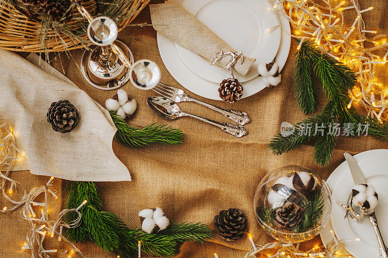 圣诞餐桌摆设。新年装饰:冷杉球果和树枝、棉球、花环和银餐具。