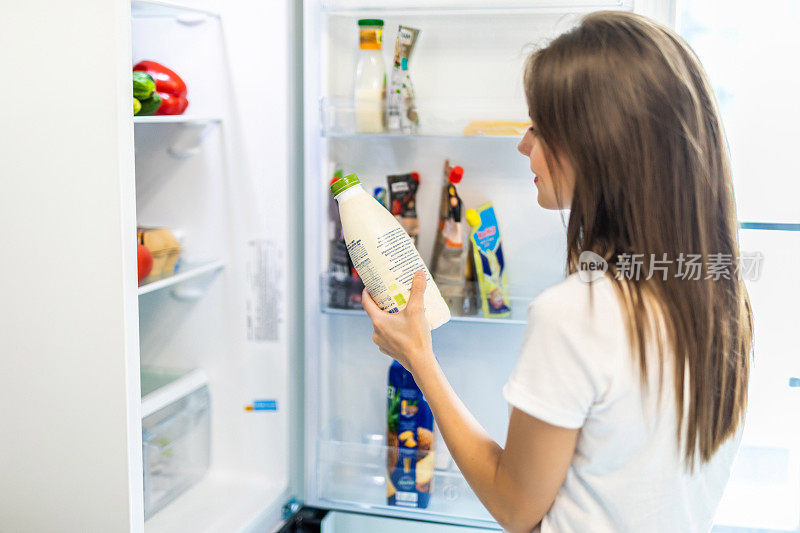 女人选择牛奶放在打开的冰箱里，冷藏新鲜可口的有机营养冰箱，女人准备做饭。健康饮食的概念