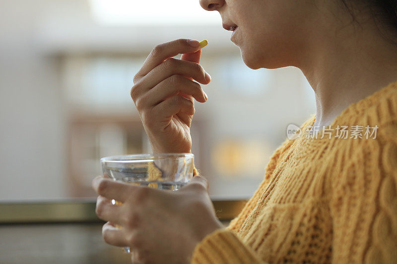 年轻女子拿着药丸和一杯水