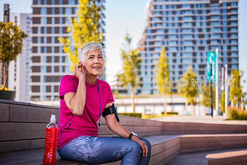 骄傲的女人在户外跑步后坐着休息时戴着耳机听音乐。