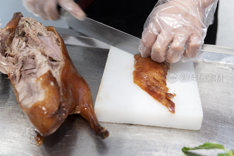 一位厨师在一家餐馆的厨房里切着美味的北京烤鸭