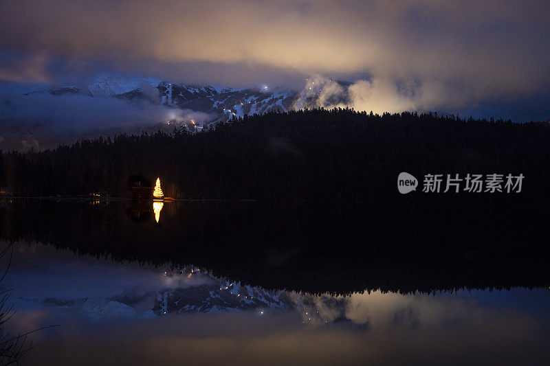 圣诞树灯倒映在湖与山景。