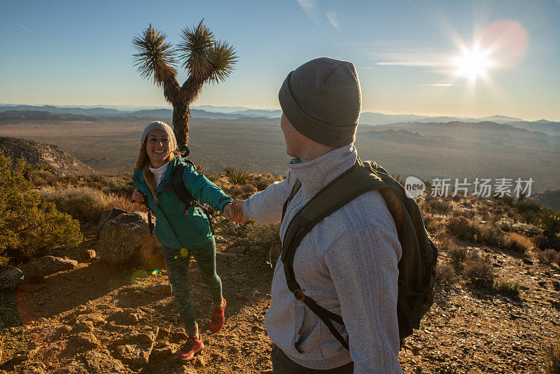 日出时分，徒步旅行者到达山顶，女人用手拉住男人