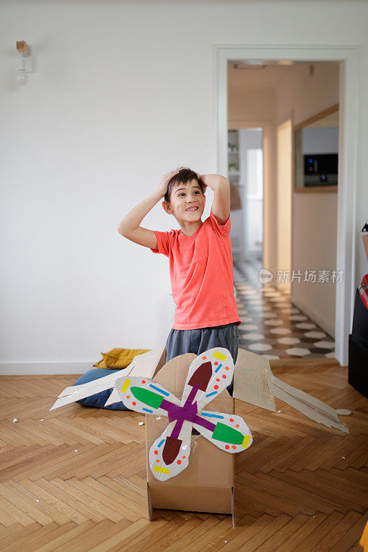 快乐的男孩站在纸板做的飞机模型中，举起手臂想象