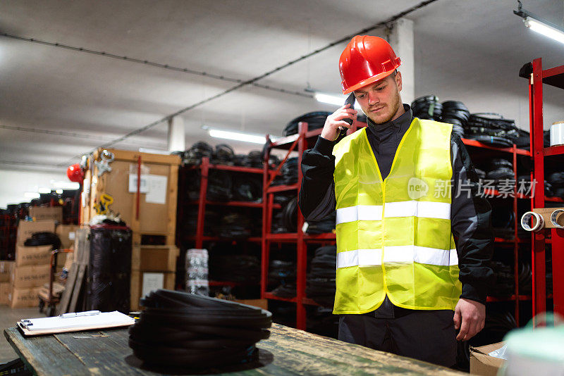 一名年轻的男性工程师在仓库里用智能手机与客户交谈