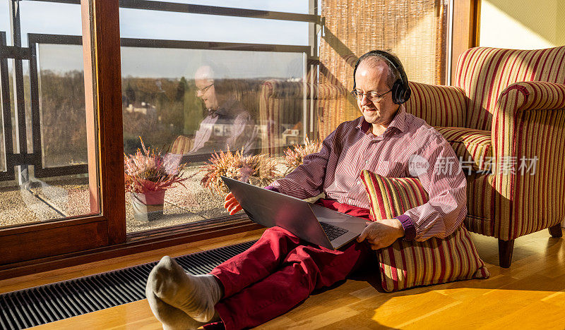 一位中年白人老人坐在客厅里，靠在有靠垫的扶手椅上，试着用笔记本电脑上网约会