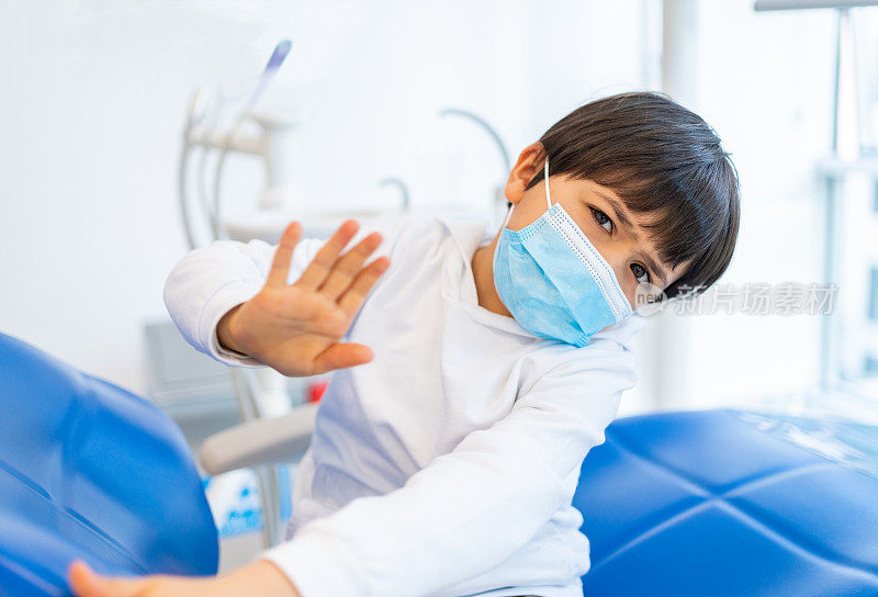 一位戴着防护口罩的小男孩病人正在牙科诊所等候牙科治疗。
