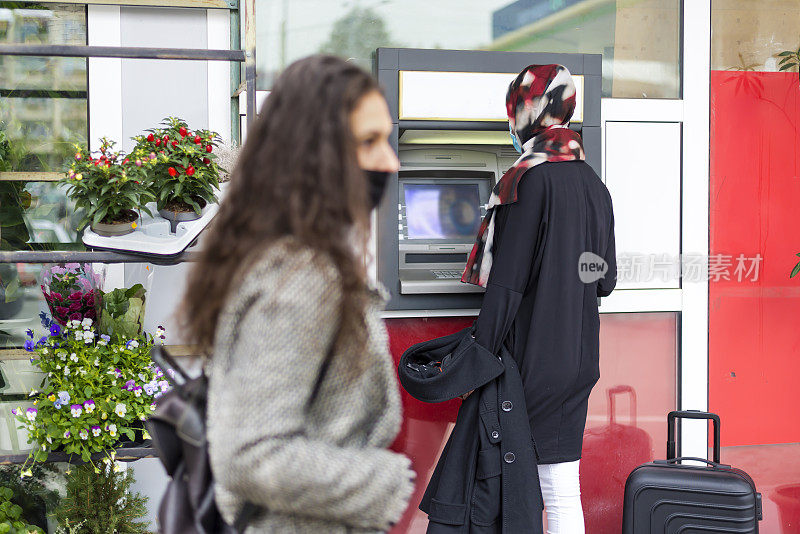 两个有着不同宗教信仰的女朋友站在自动取款机前。