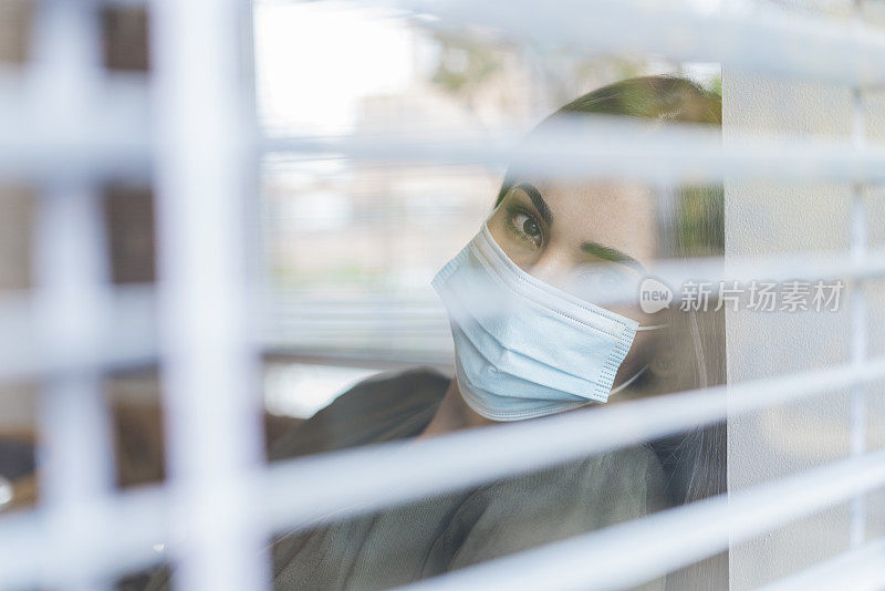 一名女性坐在餐厅的椅子上，无聊地看着窗外，因为她感染了新冠病毒，为了防止传播，不得不戴上口罩进行隔离