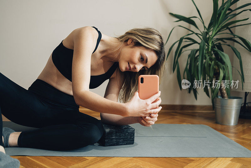 健康女性坐在瑜伽垫上，用手机拍照