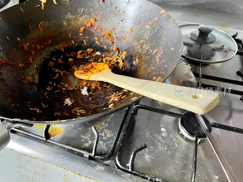 木勺放在空锅里，上面盖着烧焦的食物，煎锅放在煤气灶上，聚焦前景