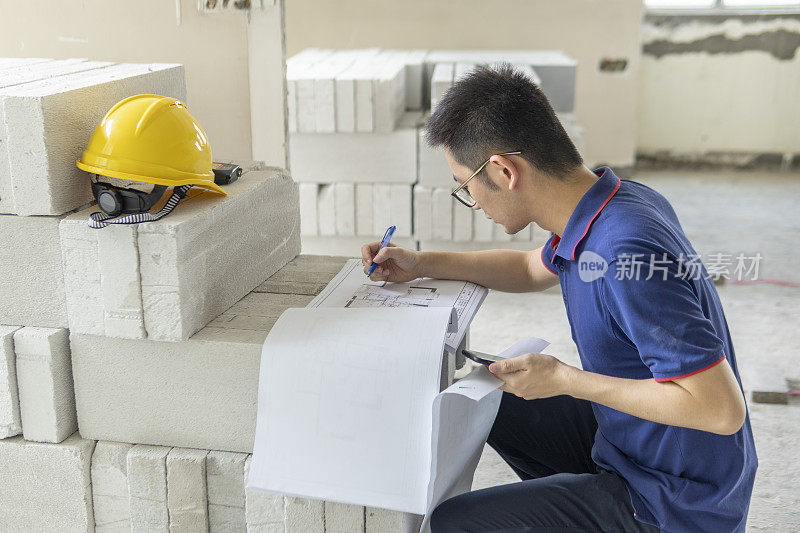 亚洲男性工程师，在装修工地处理建筑图纸和手机