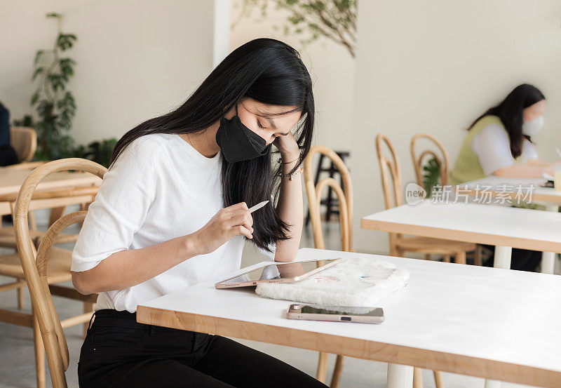 亚洲年轻女学生坐在桌旁，使用平板电脑学习