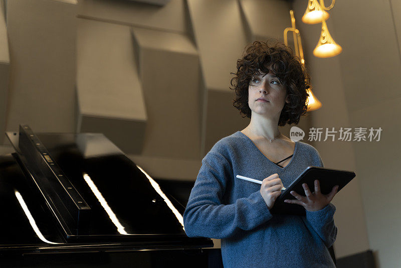 一头卷发的年轻女子倚在一架大钢琴上，想着该写些什么